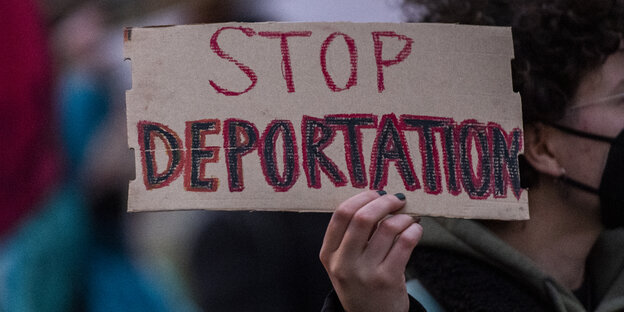 Ein Mensch hält ein Pappschild in der Hand, auf dem "Stop Deportation" steht