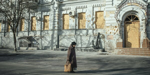 Eine alte Frau geht an einem durch Artilleriebeschuss beschädigten Gebäude vorbei