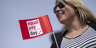 Eine Frau mit Sonnenbrille, vor ihr ist ein kleines Fähnchen zu sehen mit dem Text "equal pay day"