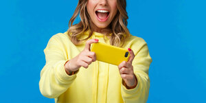 Eine Person lacht über ein Video, sie ist gelb gekleidet, der Hintergrund ist blau