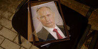 auf einem Stuhl liegt ein Putin-Porträt , das Glas ist zersplittert