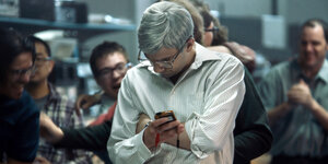 Ein Mann blickt auf sein Smartphone, jubelnde Männer im Hintergrund