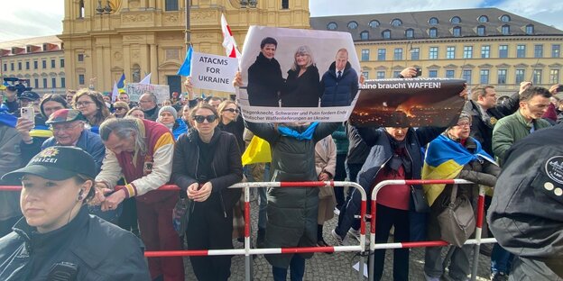 Frau hält Plakat mit den Bildern von Wagenknecht, Schwarzer und Putin hoch. Auf deren Stirnen steht ein "Z"