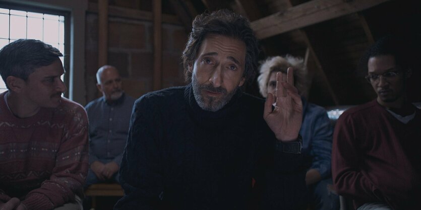 Adrian Brody im Vordergrund, andere Männer hinter ihm in einem Raum mit wenig Licht