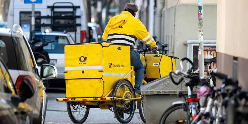 Ein Briefträger fährt mit seinem Fahrrad eine Straße entlang