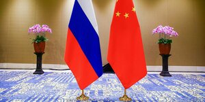Ei e russische und eine chinesische Flaggen stehen auf einem blau-gemusterten Teppich - im Hintergrund zwei Blumentöpfe symetrisch zu den Flaggen angeordnet