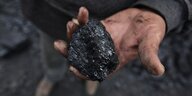 Eine Bergarbeietr hält ein Stück Kohle in den Händen