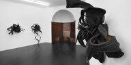 Ausstellungsansicht. Rechts vorne im Bild hängt eine organisch geformte Skulptur aus Autoreifen von Chakaia Booker