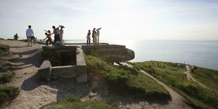 Kinder schauen durch Ferngläser , sie stehen auf Bunkeranlagen, davor das Meer