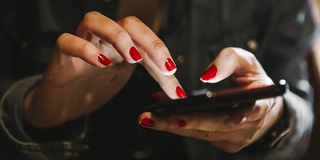 Frauenhände mit rot lackierten Fingernägeln halten ein Smartphone