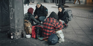 Zwei Streetworker beugen sich auf einem öffentlichen Platz zu zwei anderen Menschen herunter, die offenbar obdachlos sind