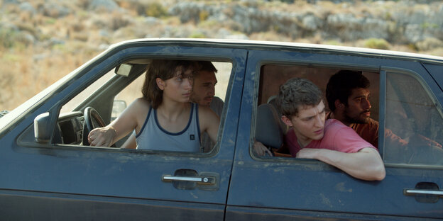 Vier junge Leute sitzen in einem Auto und blicken nach hinten, es ist heiß.