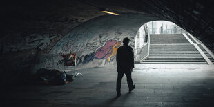 Unter einer Brücke in der Nähe des Alexanderplatzes läuft ein Passant am Hab und Gut eines Obdachlosen vorbei