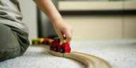 Ein Kind sitzt auf einem Teppich und schiebt die Lokomotive einer Holzeisenbahn vorwärts