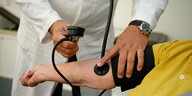Ein Hausarzt misst in seiner Praxis einer Patientin den Blutdruck