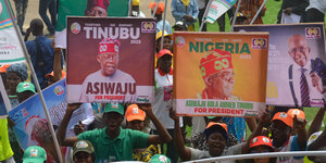 Menschen in Nigeria halten Wahlplakate des Kandidaten Tinubu hoch