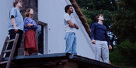 Vier Menschen stehen auf einem Hausdach und schauen in den Himmel