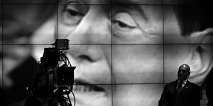Das Gesicht von Berlusconi ist auf einer riesigen Leinwand zu sehen, davor stehen ein Mann und eine Kamera