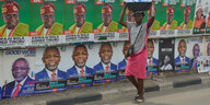Eine Frau läuft mit einer Schlüssel auf dem Kopf vor einer Wand mit Wahlplakaten