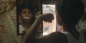 Ein indischer Junge mit Rasierschaum über der Lippe schaut sich im Spiegel an