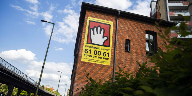 An einem Backsteingebäude hängt ein Plakat mit der Aufschrift: "Kindernotdienst 61 00 61 Rund um die Uhr erreichbar".