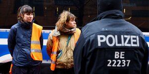 Das Bild zeigt einen Polizisten und festgenommene Aktivistinnen bei einem Klimaprotest für eine Geschwindigkeitsbegrenzung.