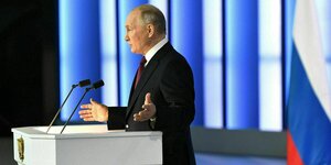Putin steht an einem Rednerpult und gestikuliert mit beiden Händen