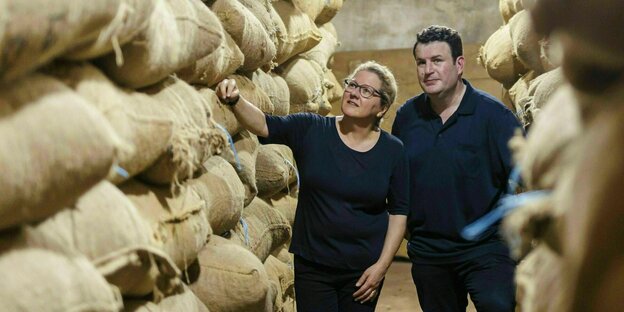 Svenja Schulze und Hubertus Heil stehen zwischen meterhohen aufgetürmten Säcken mit Kakao