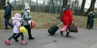 Eine Frau und zwei Kinder in Winterkleidung schleppen ihr Gepäck auf einem Fussweg