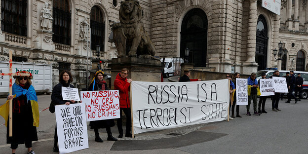 Menschen protestieren vor der Wiener Hofburg. Auf einem Transparent ist der Satz "Russia is a Terrorist State" zu lesen
