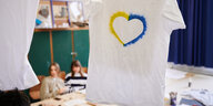 Blick auf T-Shirt mit Herz in ukrainischen Farben, im Hintergrund ein Klassenzimmer