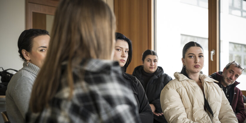 Schülerinnen und ihre Lehrer:innen sitzen in einem Stuhlkreis