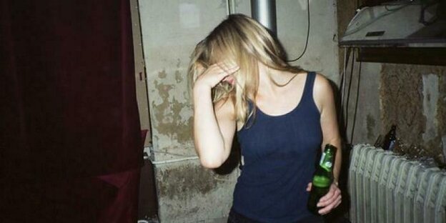 eine junge Frau mit Bierflasche in der Hand hält ihre Hand vor das Gesicht