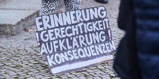 Ein Plakat auf einer Straße. Darauf steht "Erinnerung, Gerechtigkeit, Aufklärung, Konsequenzen"