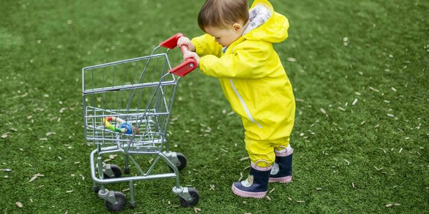 Ein Kleinkind schiebt einen Spielzeug EInkaufswagen