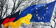 Die Flaggen der Bundesrepublik Deutschland, der Ukraine und der Europäischen Union wehen vor dem Schloss Bellevue während der zentralen deutschen Veranstaltung am Jahrestag des russischen Überfalls auf die Ukraine im Wind
