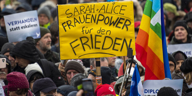 Ein Teilnehmer einer Demonstration für Verhandlungen mit Russland am Brandenburger Tor hält ein Plakat mit der Aufschrift "Sarah + Alice - Frauenpower für den Frieden"