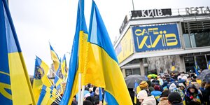 Teilnehmer einer Demonstration mit ukrainischen Fahnen stehen an der Berliner Karl-Marx-Allee vor dem Cafe Moskau, das für ein paar Tage in Cafe Kyiv (Kiew) umbenannt wurde