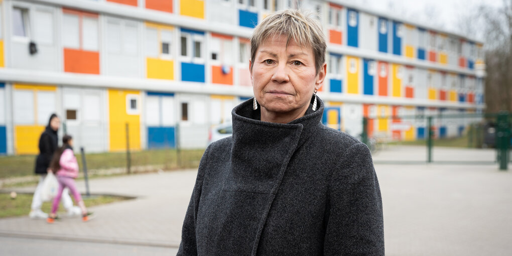 Elke Breitenbach steht in dunklem Mantel vor einer bunten Containerunterkunft