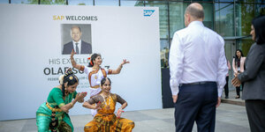 Drei indische Tänzerinnen empfangen den Kanzler Olaf Scholz in der indische Niederlassung des deutschen Unternehmens SAP. Scholz ist nur von hinten zu sehen.
