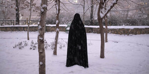 Eine Frau im Ganzkörperschleier steht als schwarze Gestalt im Schnee