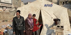Menschen vor einem Zelt in einer städtischen Trümmerlandschaft