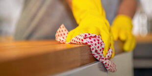 Gelbe Gummihandschuhe wischen mit einem Putzlappen mit roten Punkten