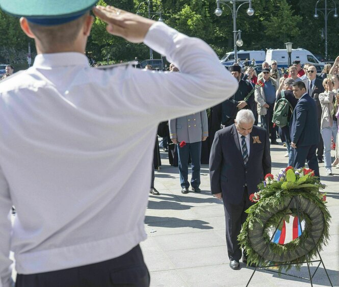 Sergei Nechaev verneigt sich vor einem Kranz, im Vordergrund salutiert ein russischer Soldat