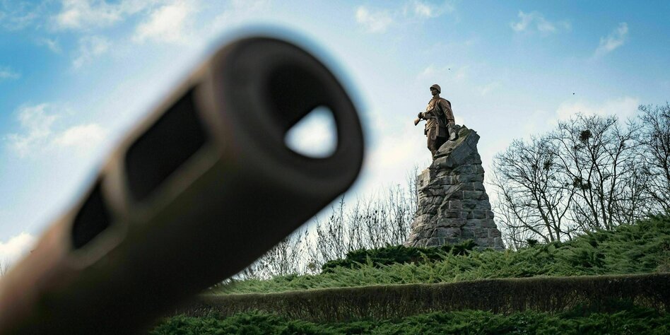 Das Zielrohr eines Panzers schiebt sich ins Bild, im Hintergrund das Denkmal, das einen russischen Soldaten zeigt
