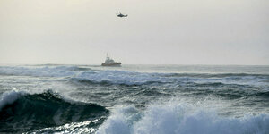 Ein Rettungsboot auf einem vom Wind aufgepeitschten Meer, darüber ein Hubschrauber