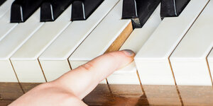 Der Zeigefinger eines Mädchen mit silbernem Nagellack drückt eine Klaviertaste herunter