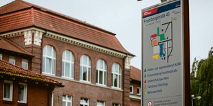 Ein rotes Klinkergebäude mit einem Lageplan-Schild davor