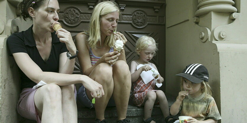 2 Fraune und 2 Kinder lutschen am Eis und sitzen in einem Hauseingang