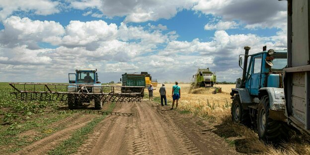 Ukranische Bauern stehen mit Erntemaschinen an einem Feldrand